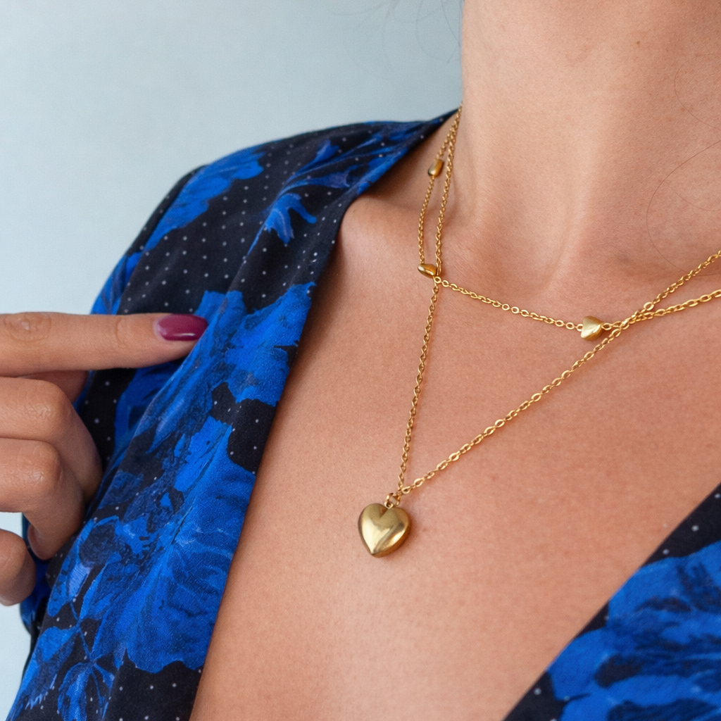 Gold heart-shaped necklace worn by a person with a blue patterned garment.